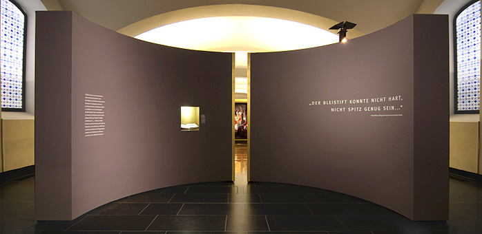 Ein Zitat und ein goldener Spalt wirken wie ein Weihebecken vor Betreten der Ausstellung